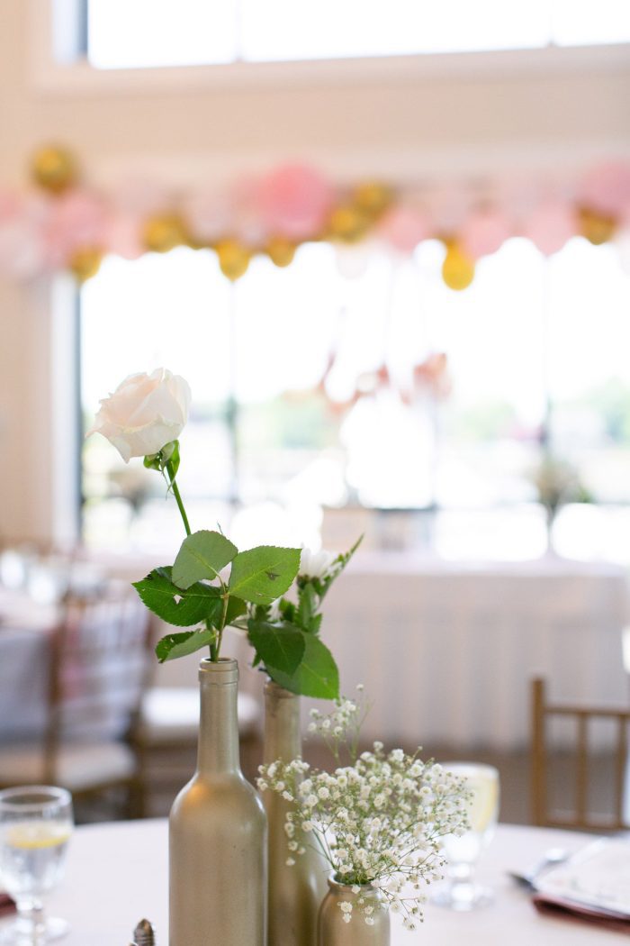 Single white roses in gold spray painted bottles as a centerpiece on a table.